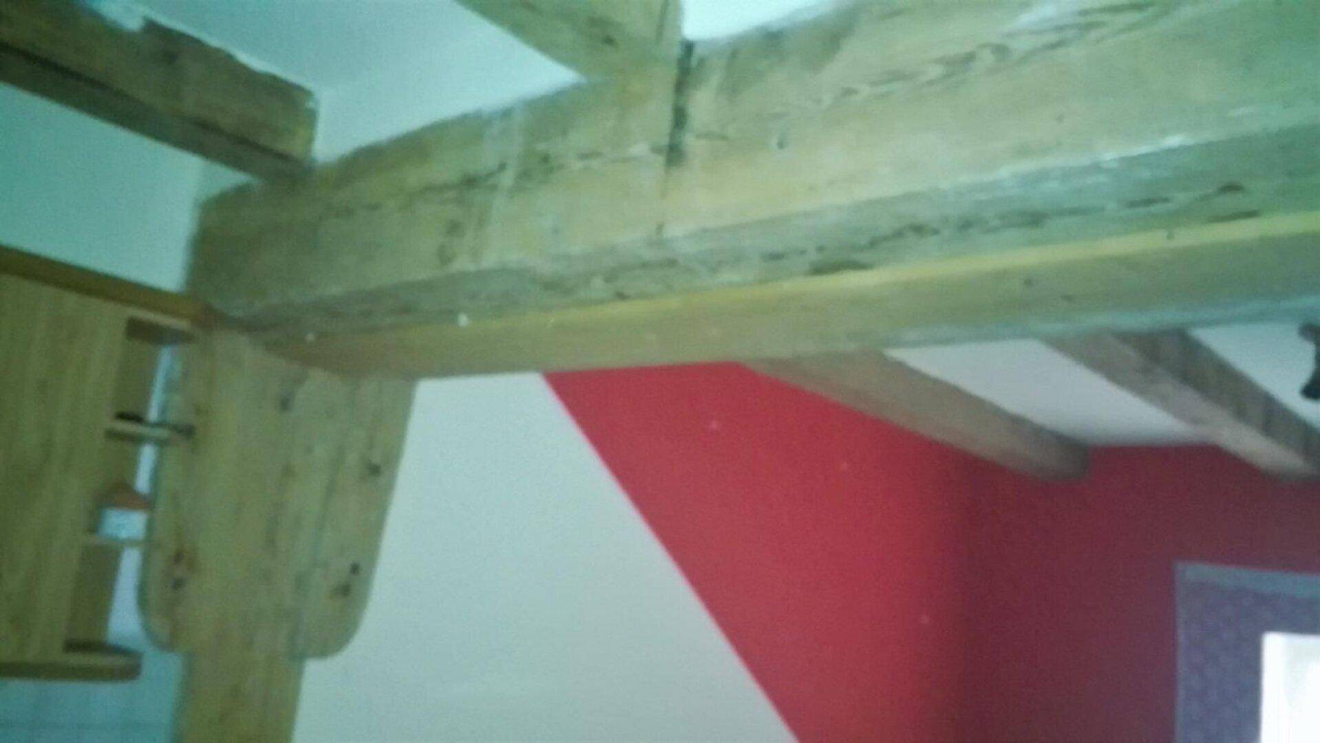 Innenraum mit sichtbaren Holzbalken an der Decke und einer markanten roten Wandfläche, die einen rustikalen Charme verleiht.