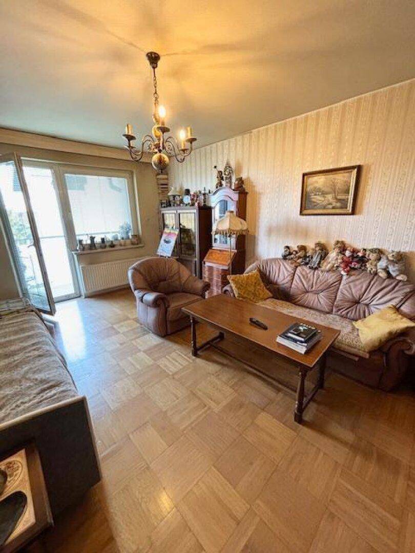 Helles Wohnzimmer mit Parkettboden, Sofa und Zugang zu einem Balkon.