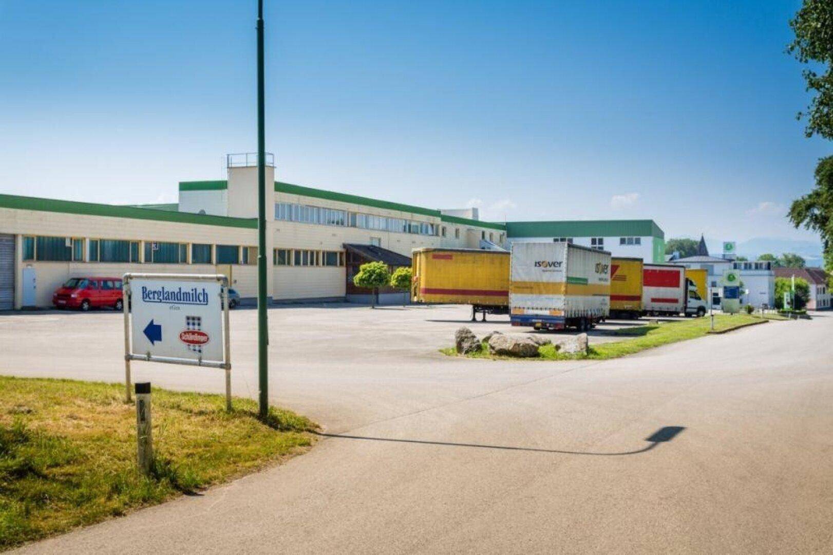 Außenansicht des Industriekomplexes mit Lastwagen auf dem Hof und einem Hinweisschild am Eingang.