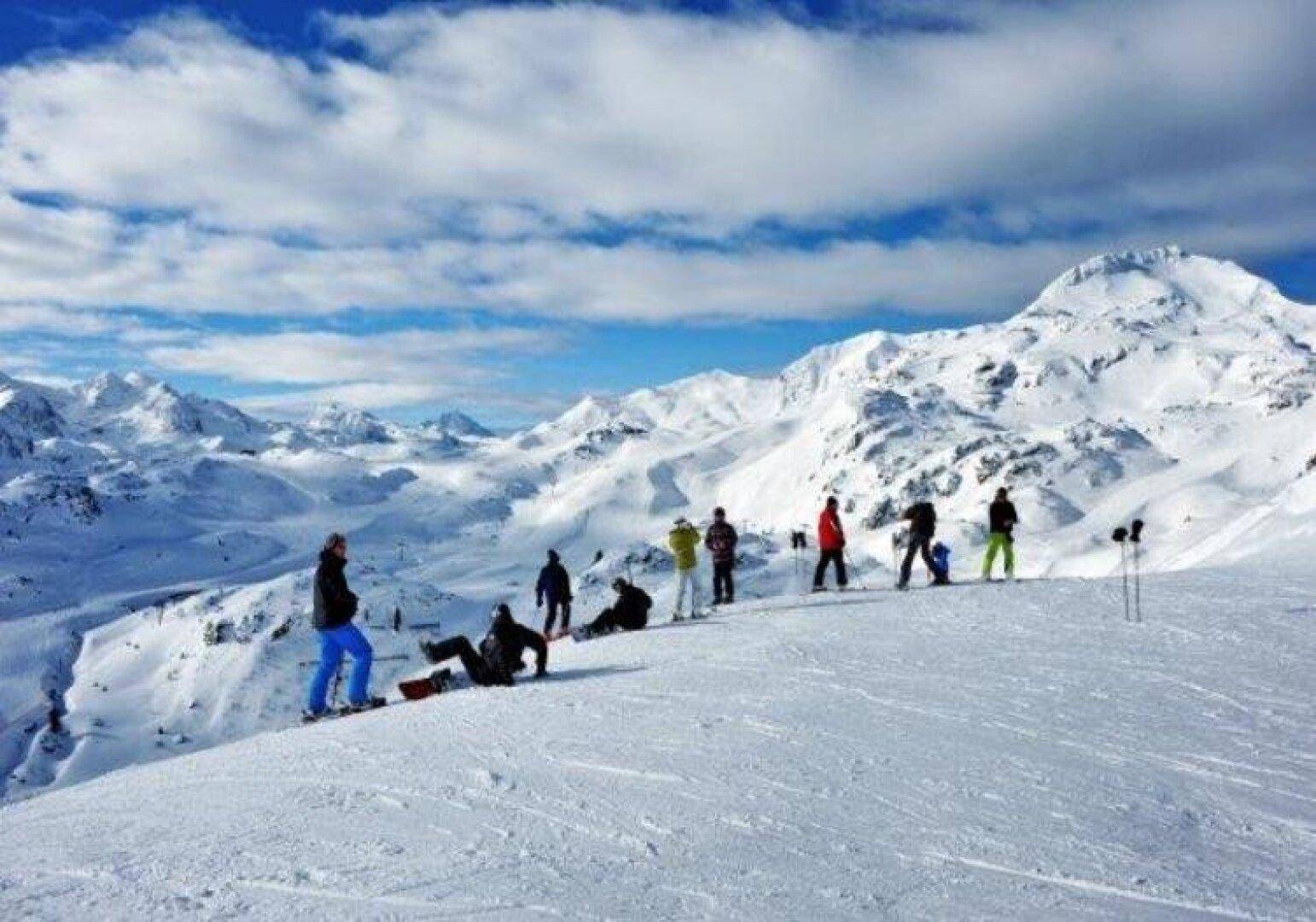 Gruppe von Menschen genießt die weite Aussicht auf die verschneite Berglandschaft unter blauem Himmel.