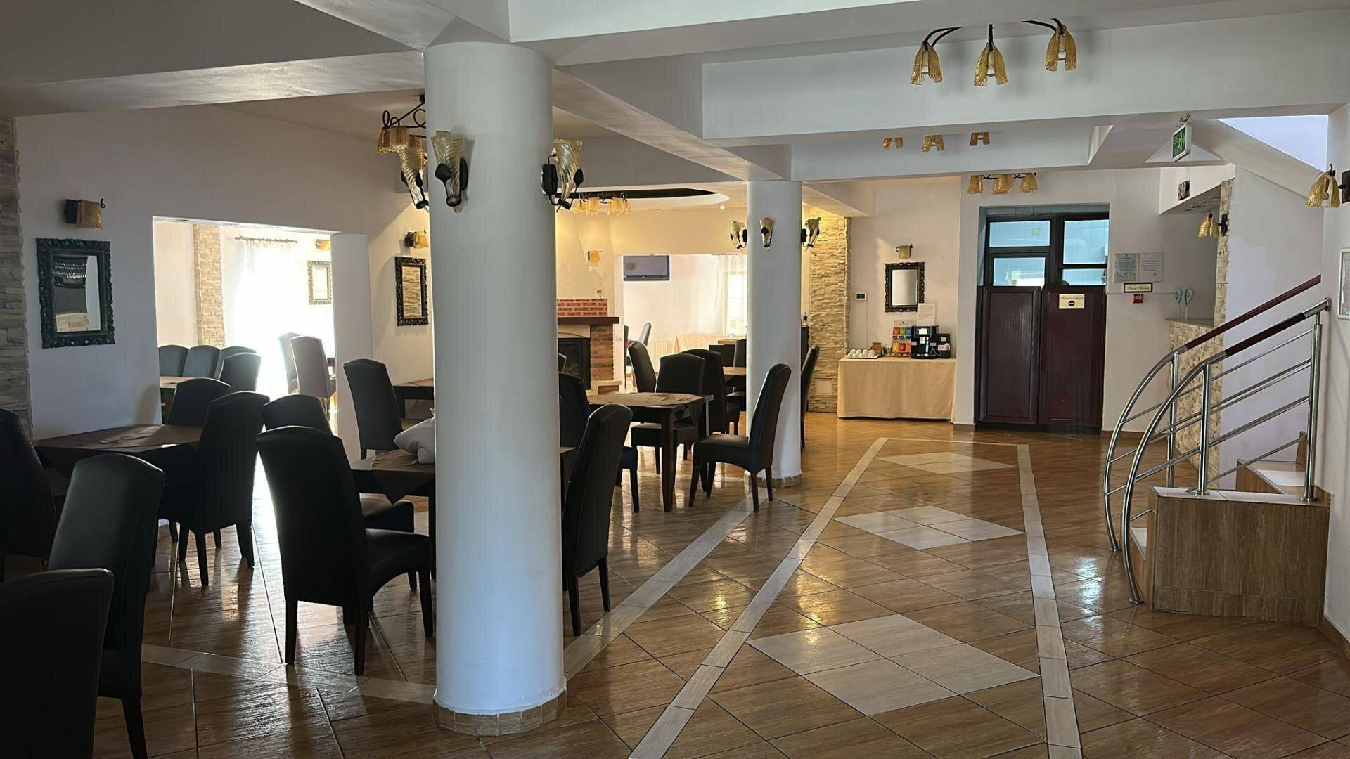 Geräumiger Speisesaal mit Säulen, Fliesenboden und mehreren Tischen mit Stühlen.