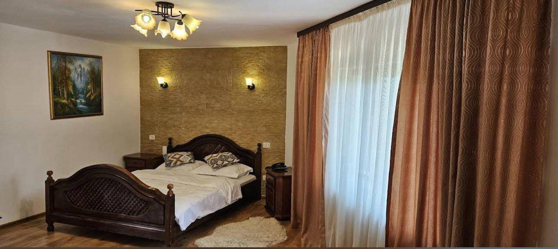 Gemütliches Schlafzimmer mit dunklem Holzrahmenbett, beiger Akzentwand und braunen Vorhängen.
