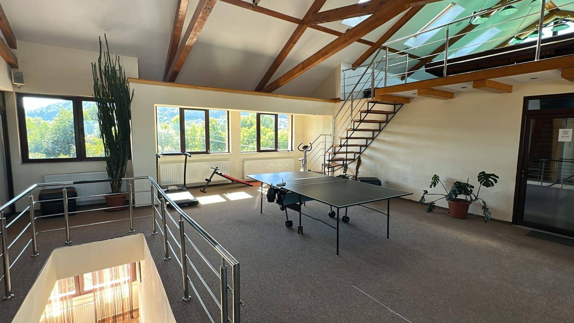 Großer Freizeitraum mit Tischtennisplatte, Fitnessgeräten und Holzbalken an der Decke.