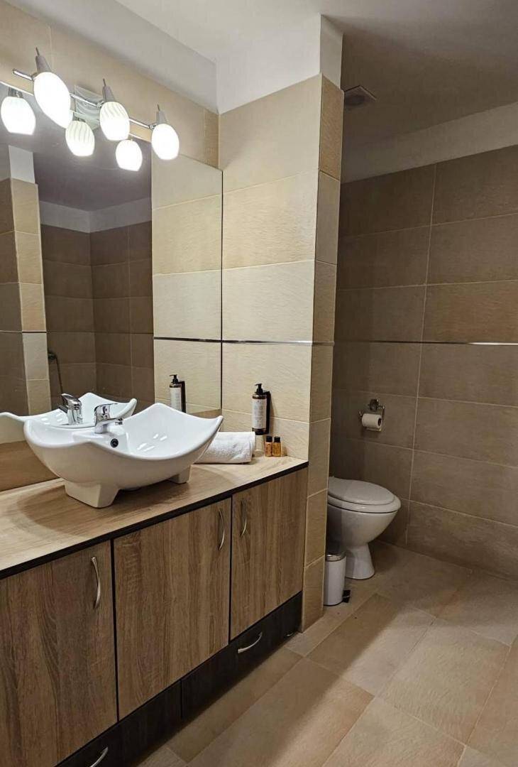 Modernes Badezimmer mit beigen Fliesen, einem einzigartigen Waschbecken und Holzunterschränken.