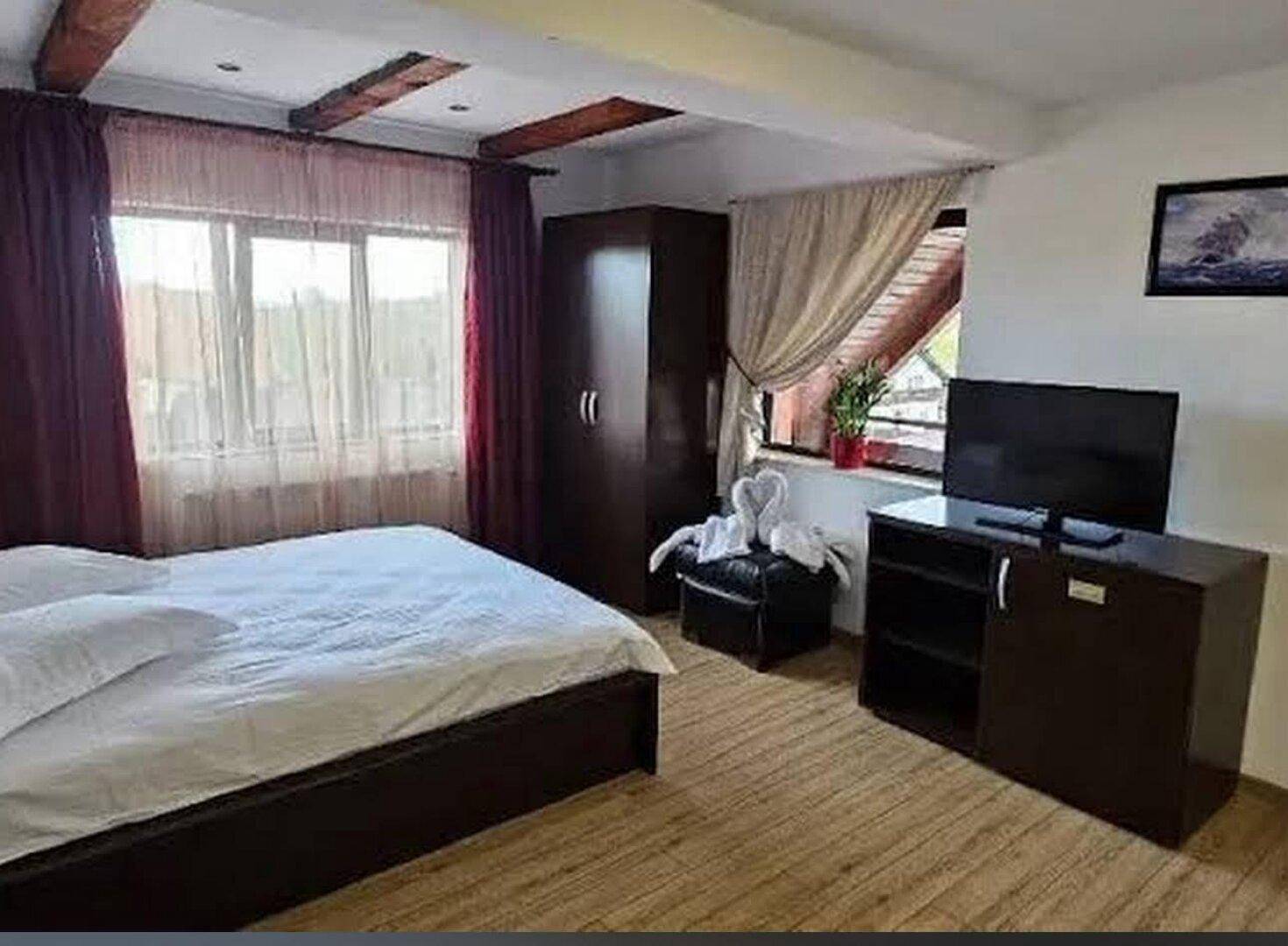 Schlafzimmer mit Holzbalken an der Decke, großem Fenster und dunklen Möbeln.