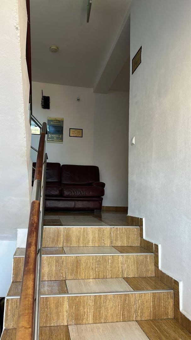 Treppenhaus mit Fliesenstufen, Holzgeländer und weiß gestrichenen Wänden.