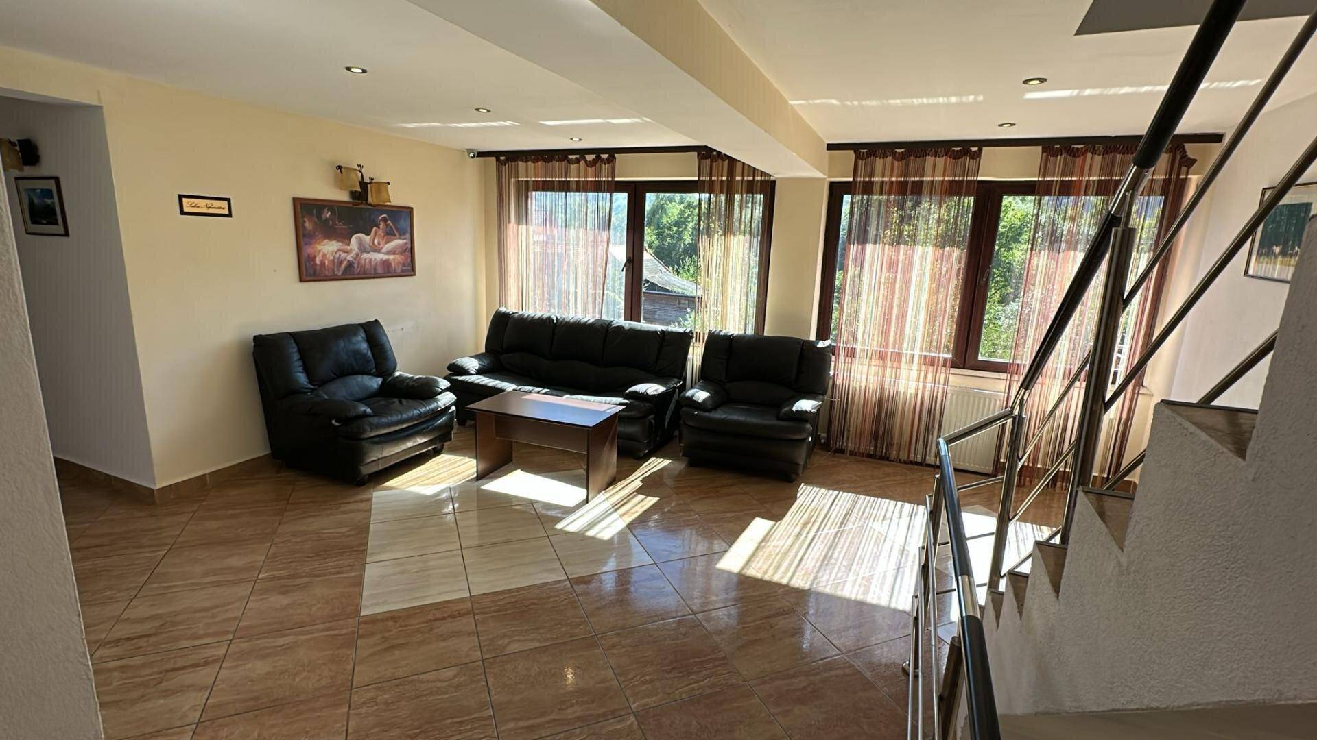 Geräumiger Wohnbereich mit Ledersofas, Fliesenboden und großen Fenstern mit Blick ins Grüne.
