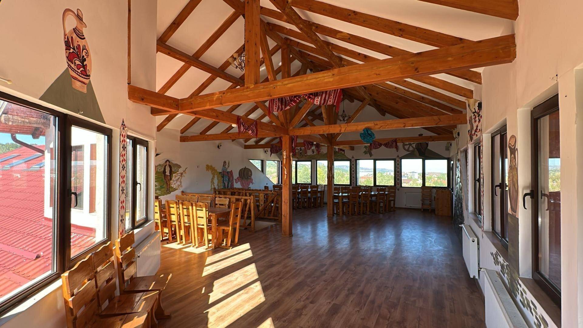 Großer Speisesaal mit Holzbalken, vielen Fenstern und Holzboden.