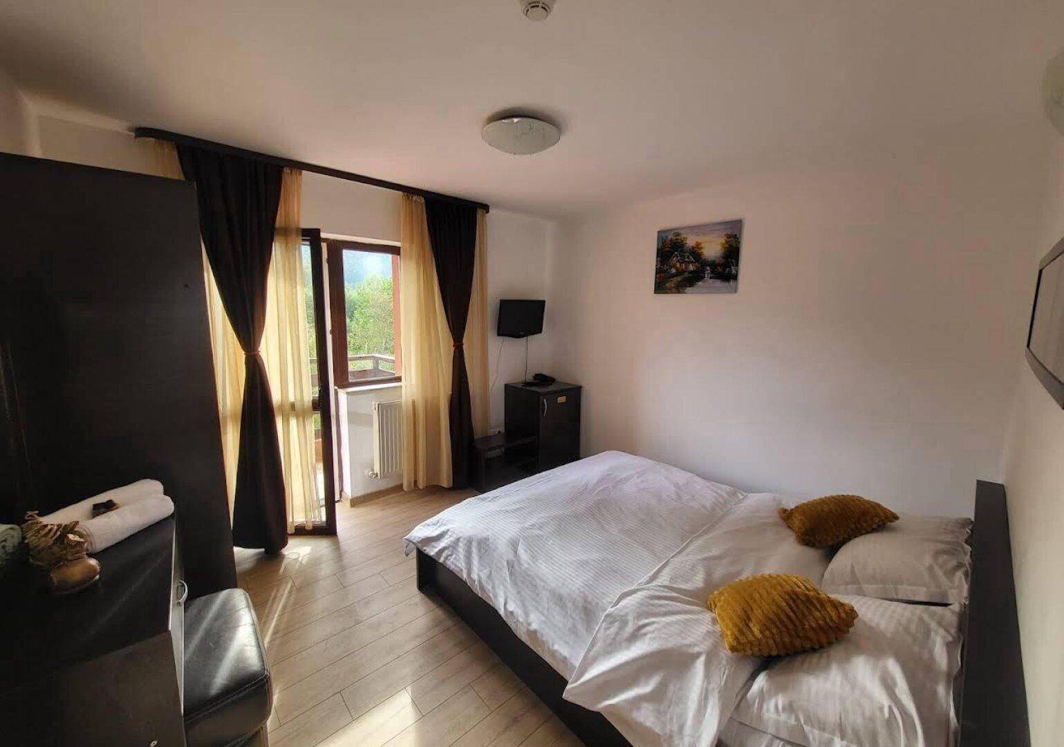 Helles Schlafzimmer mit Doppelbett, Holzboden und Zugang zu einem Balkon oder einer Terrasse.