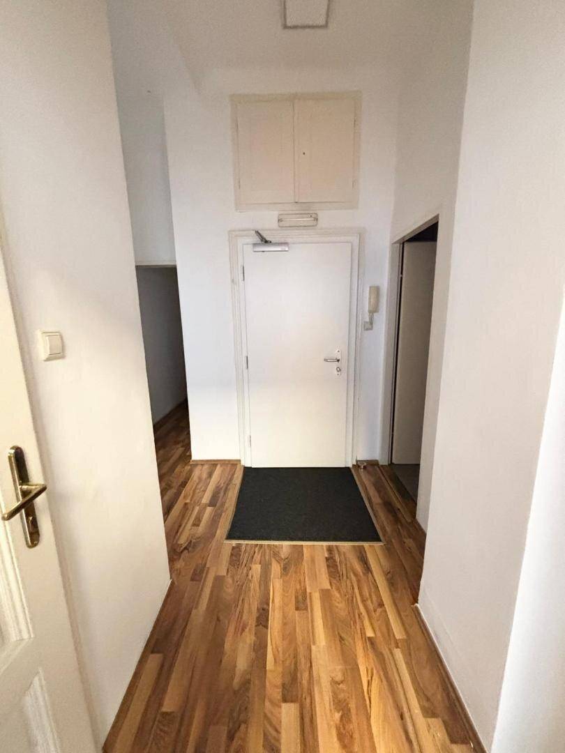 Eingangsbereich mit Holzboden, weißer Tür und einer Fußmatte.