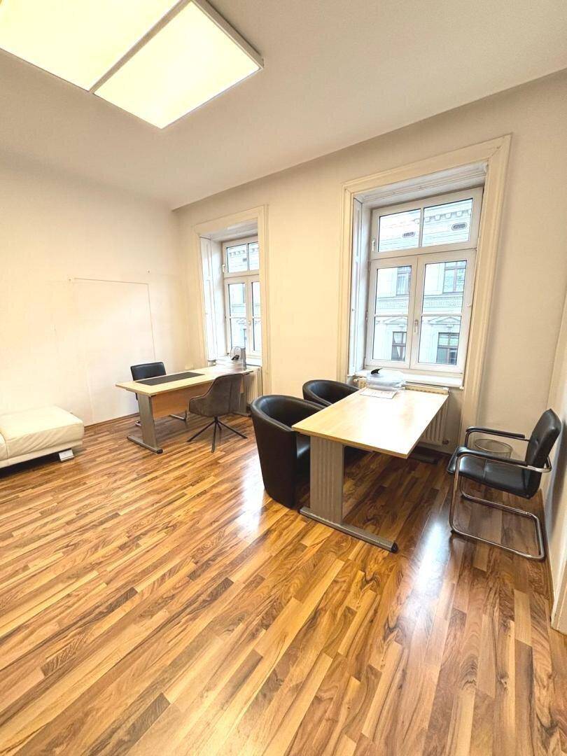 Büro mit Holzboden, zwei Arbeitsplätzen und einem weißen Sofa im Hintergrund.
