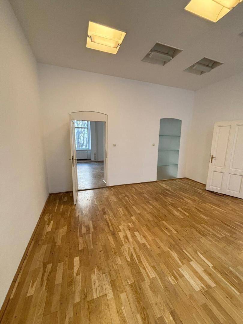 Leeres Büro mit Holzboden, weißen Wänden und zwei Türen, die zu weiteren Räumen führen.