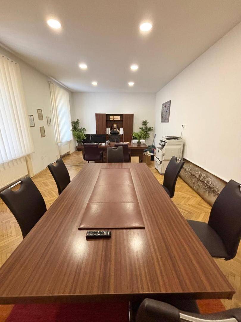 Großer Konferenzraum mit Holzboden, langem Tisch und Stühlen, umgeben von Pflanzen.