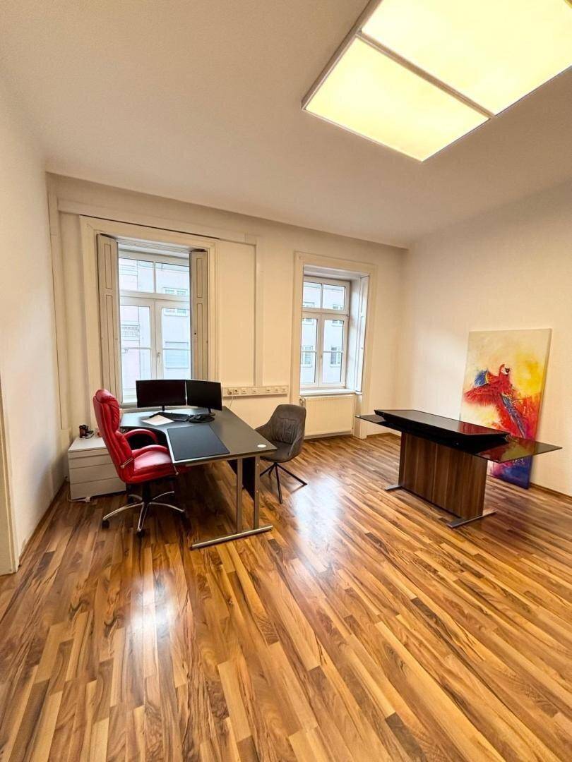 Helles Büro mit zwei modernen Arbeitsplätzen, Holzboden und farbenfroher Kunst.
