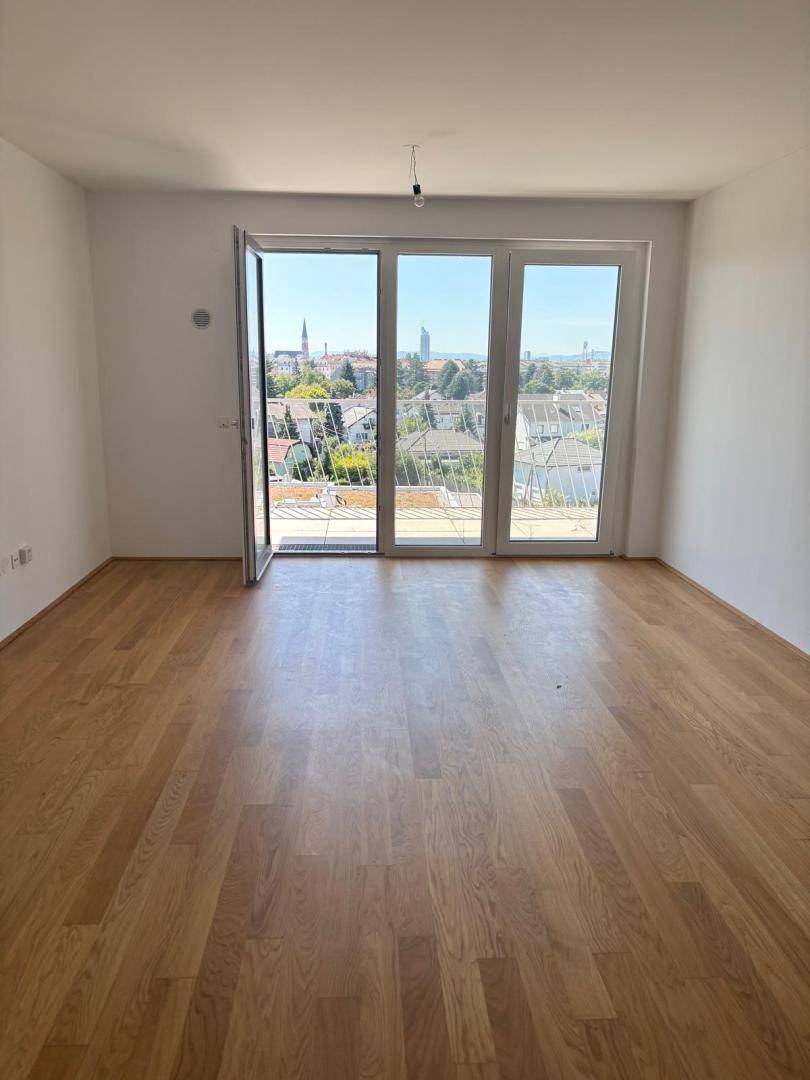 Helles Wohnzimmer mit Parkettboden und großen Fenstern, die Zugang zu einem Balkon mit Stadtblick bieten.
