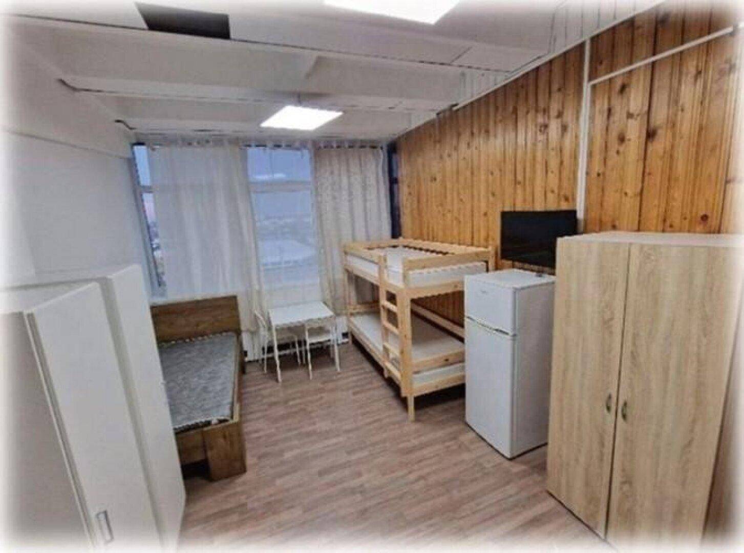 Schlafzimmer mit Etagenbett, Einzelbett, Kleiderschrank und Kühlschrank, mit Holzwandverkleidung.