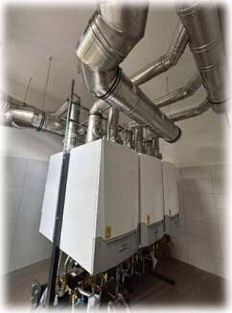 Technikraum mit großen Heizungsanlagen und sichtbaren Lüftungsrohren unter der Decke.