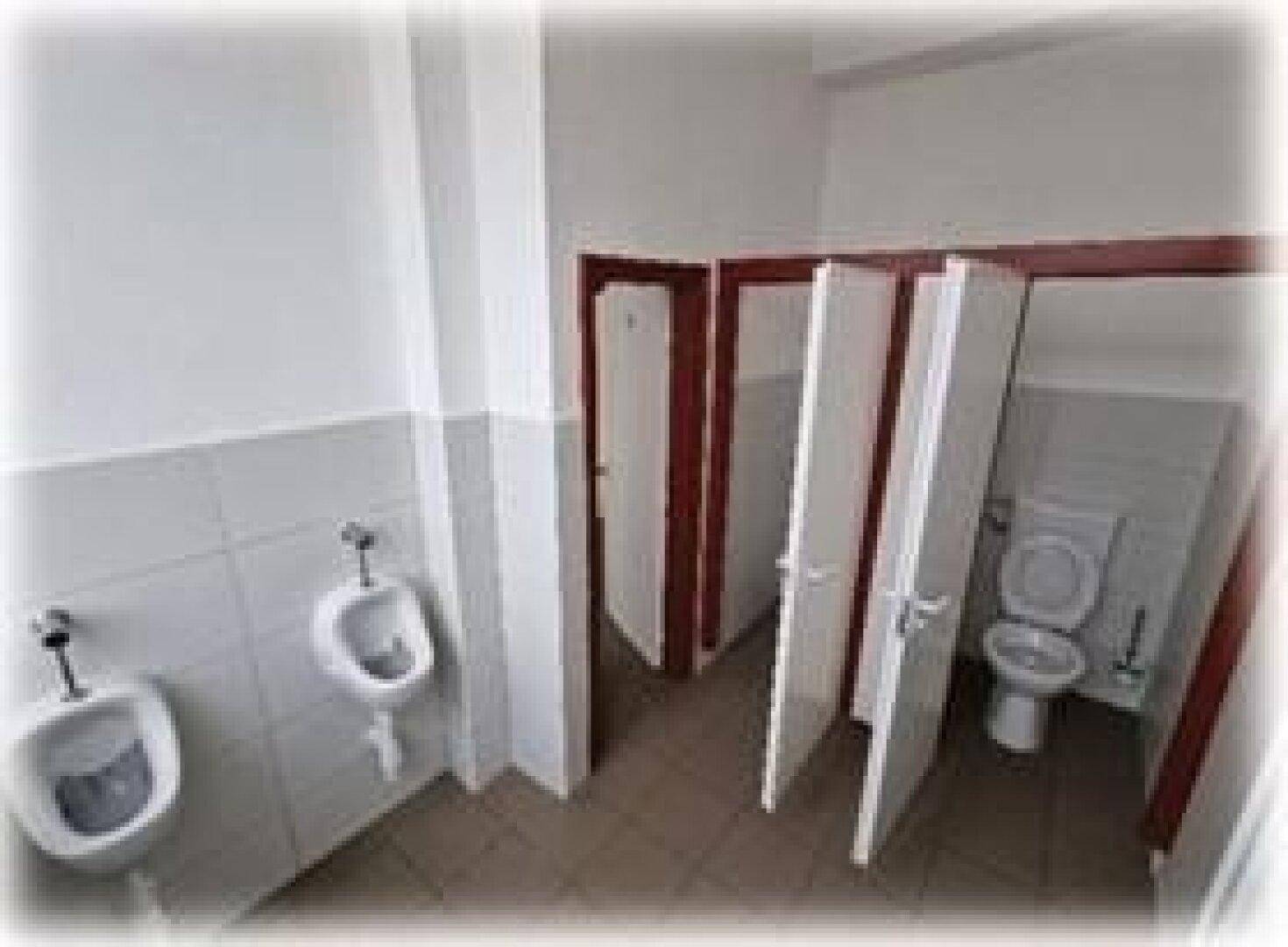 Öffentliche Toilettenanlage mit Urinalen und mehreren Kabinen, mit Fliesen an Wänden und Boden.