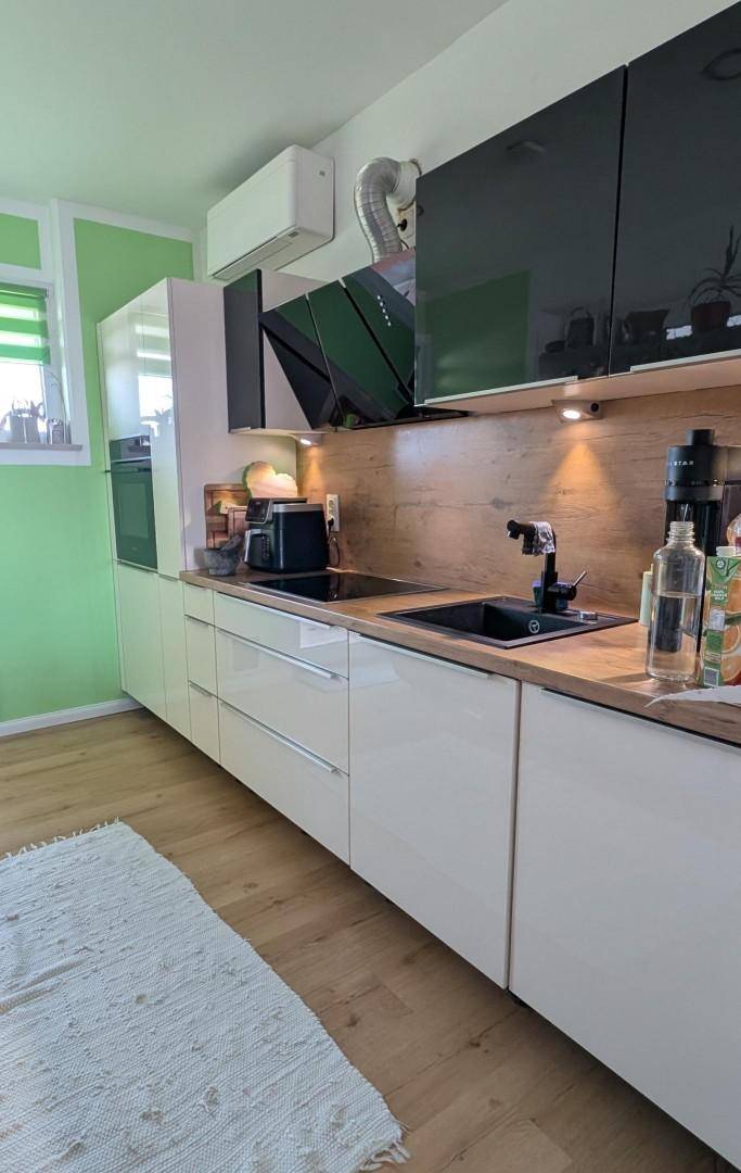 Moderne Küche mit weißen Hochglanzfronten, Holzarbeitsplatte, Induktionskochfeld und grüner Wand.