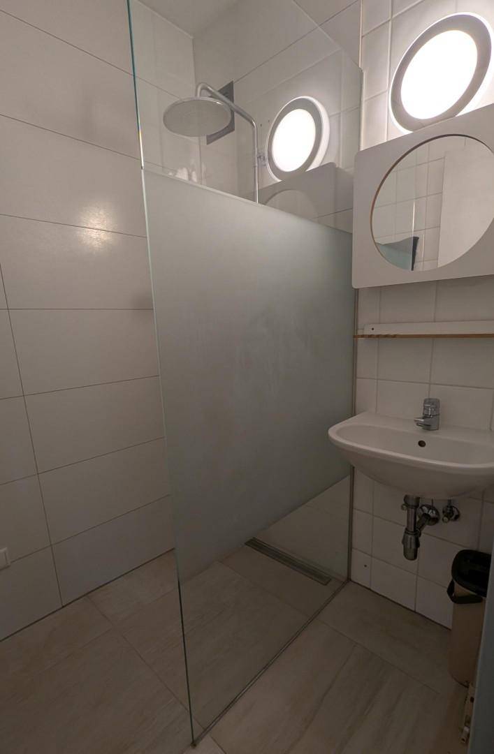 Modernes Badezimmer mit Duschkabine, Waschbecken und runden Fenstern.