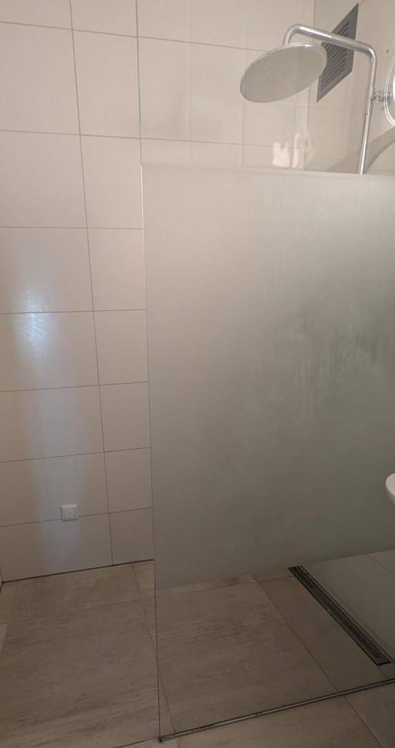 Duschbereich mit Glaswand, Regendusche und weißen Fliesen im modernen Badezimmer.