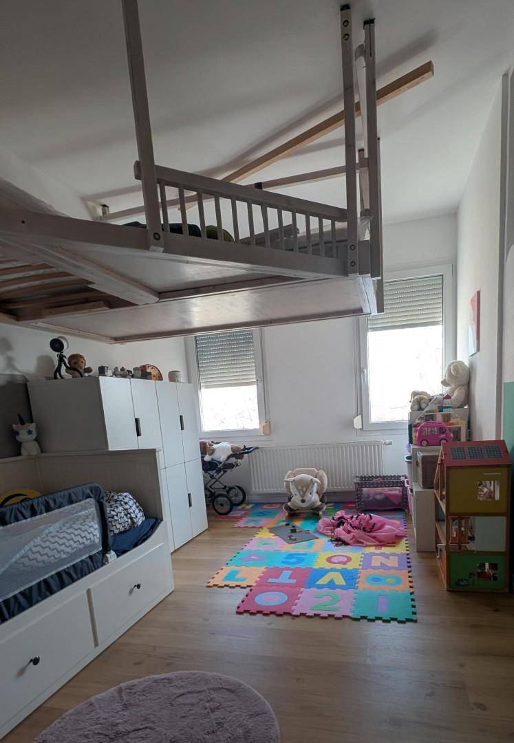 Geräumiges Kinderzimmer mit Hochbett, Spielbereich und viel Tageslicht durch die Fenster.