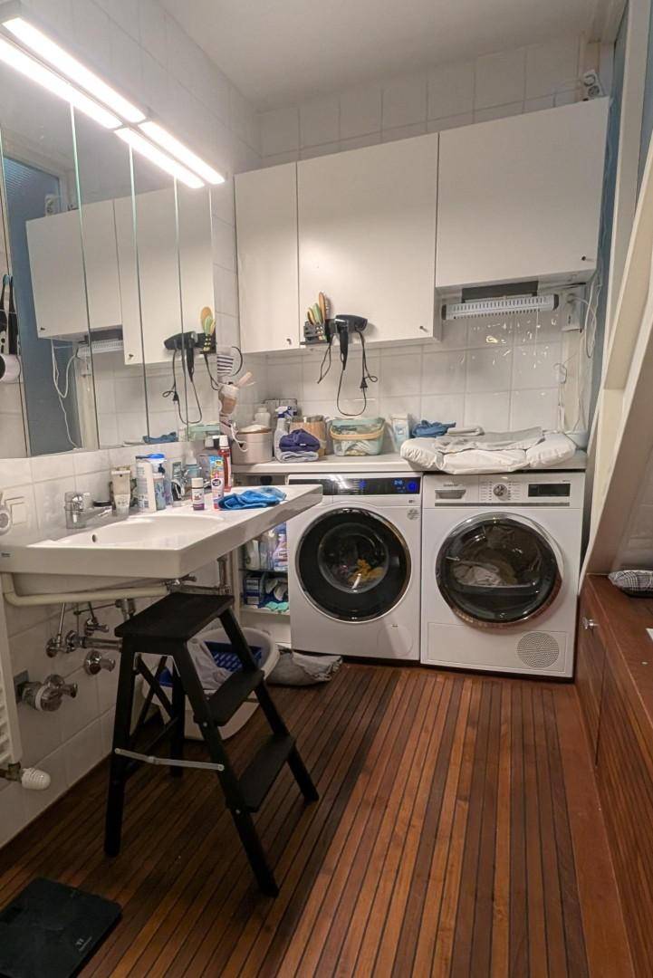Badezimmer mit Waschmaschine, Trockner, Waschbecken und Holzfußboden.