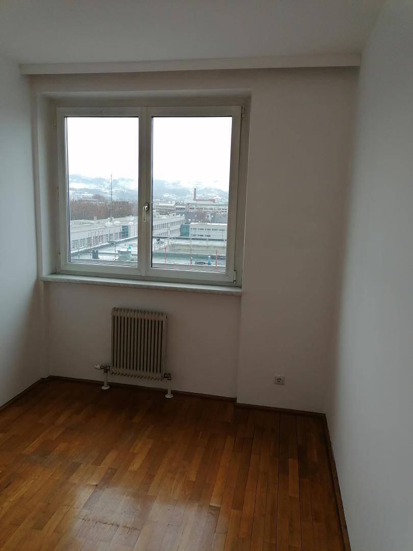 Helles Zimmer mit Holzboden und einem Fenster, das einen weiten Blick auf die Stadt ermöglicht.