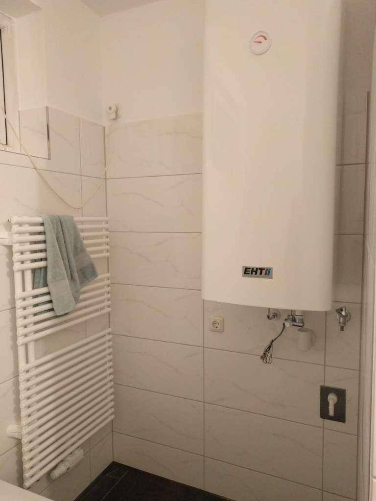 Badezimmer mit Wandfliesen, einem Warmwasserboiler und einem beheizten Handtuchhalter.