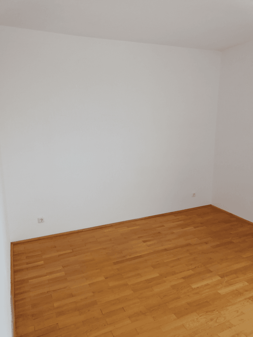 Leeres Zimmer mit hellem Holzboden und weißen Wänden, bereit zur individuellen Gestaltung.