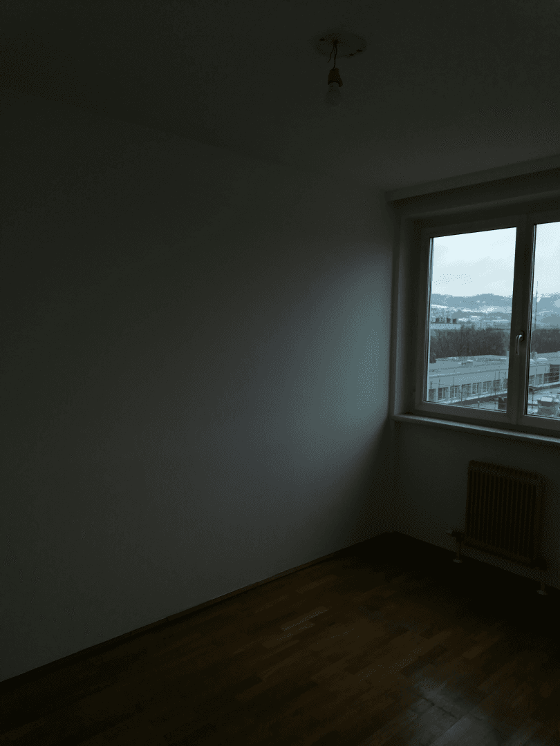 Dunkles Schlafzimmer mit Holzboden und einem Fenster, das einen Blick auf die Umgebung bietet.