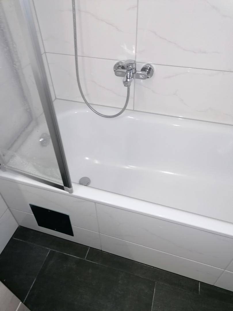 Nahaufnahme einer Badewanne mit Duscharmatur und moderner Fliesenverkleidung im Badezimmer.