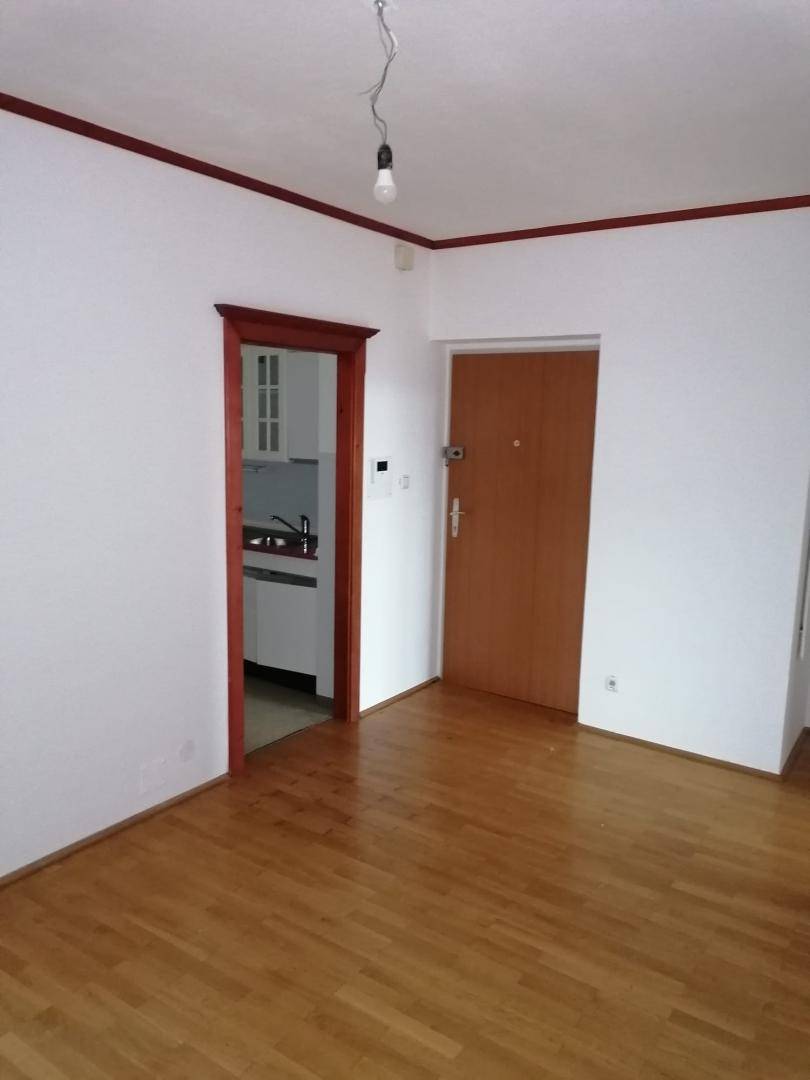 Leerer Wohnbereich mit Holzboden und Zugang zu einer kleinen Kochnische.