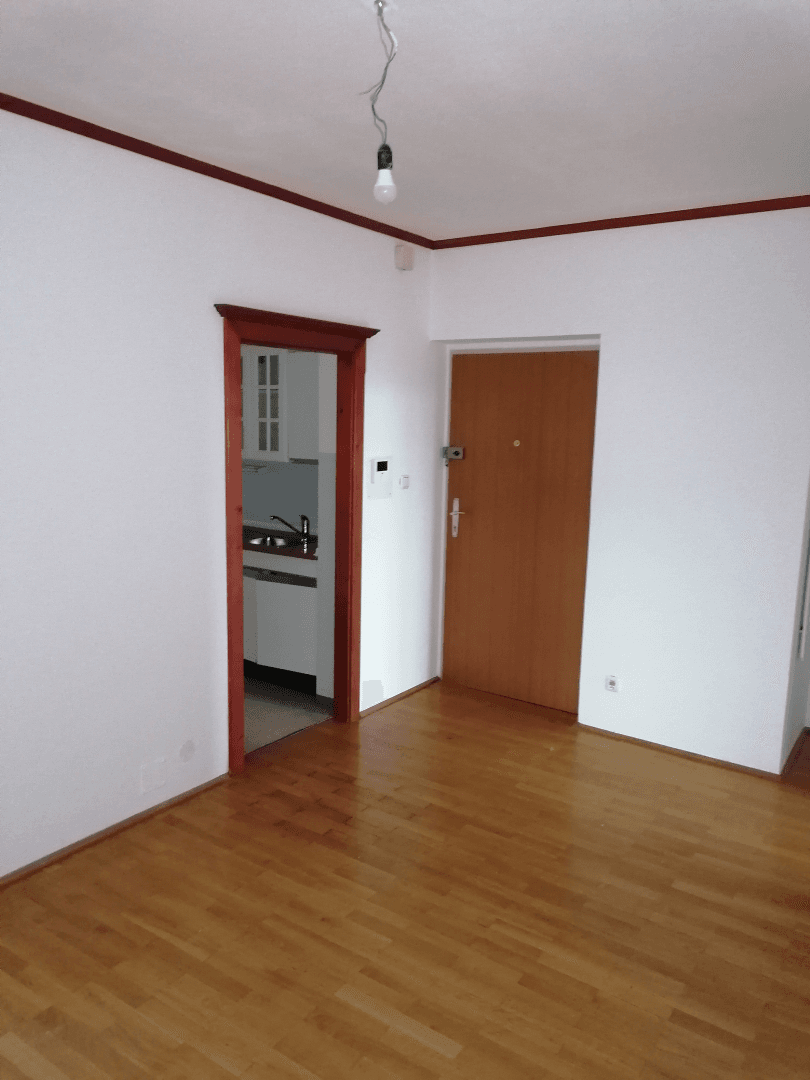 Leerer Wohnbereich mit Holzboden und Zugang zu einer kleinen Kochnische.
