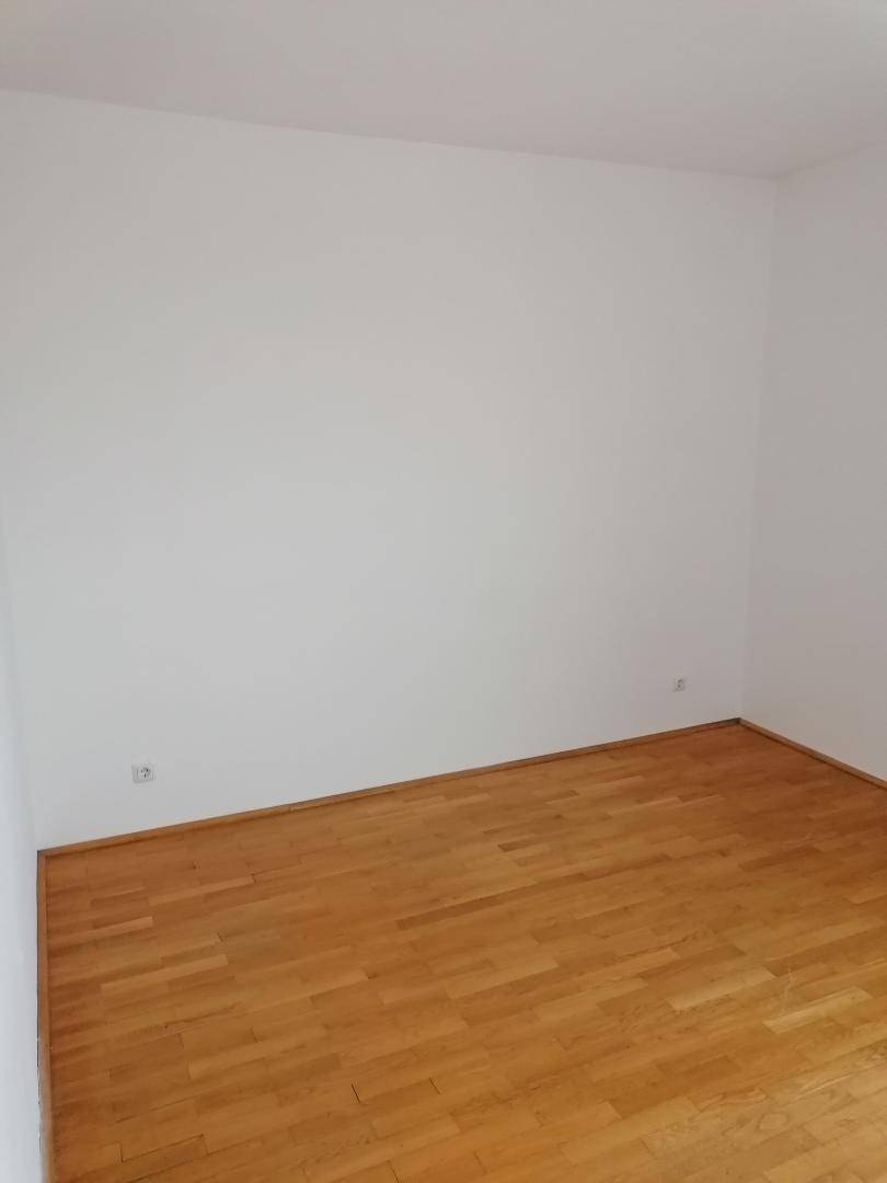 Leeres Zimmer mit hellem Holzboden und weißen Wänden, bereit zur individuellen Gestaltung.