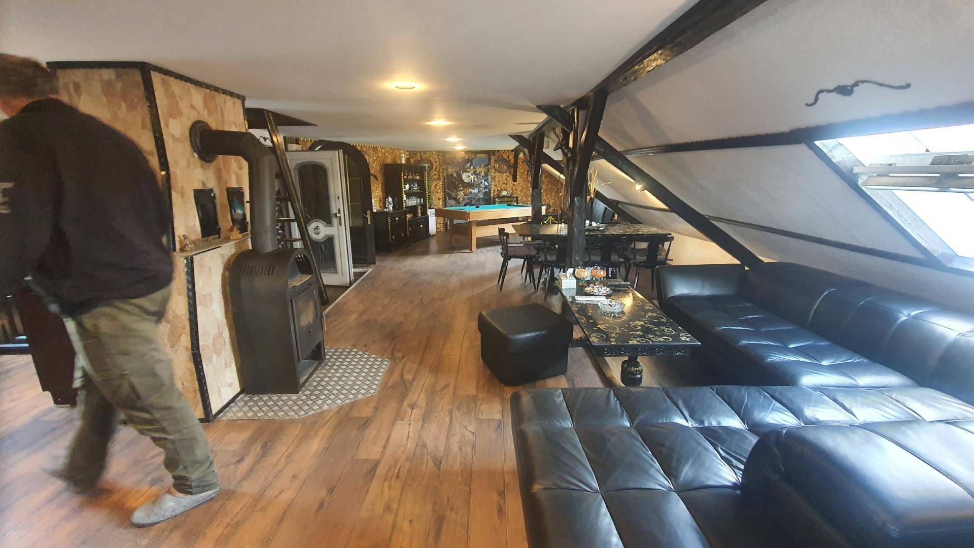 Gemütlicher Wohnbereich im Dachgeschoss mit Kaminofen, Ledersofa und Holzboden.