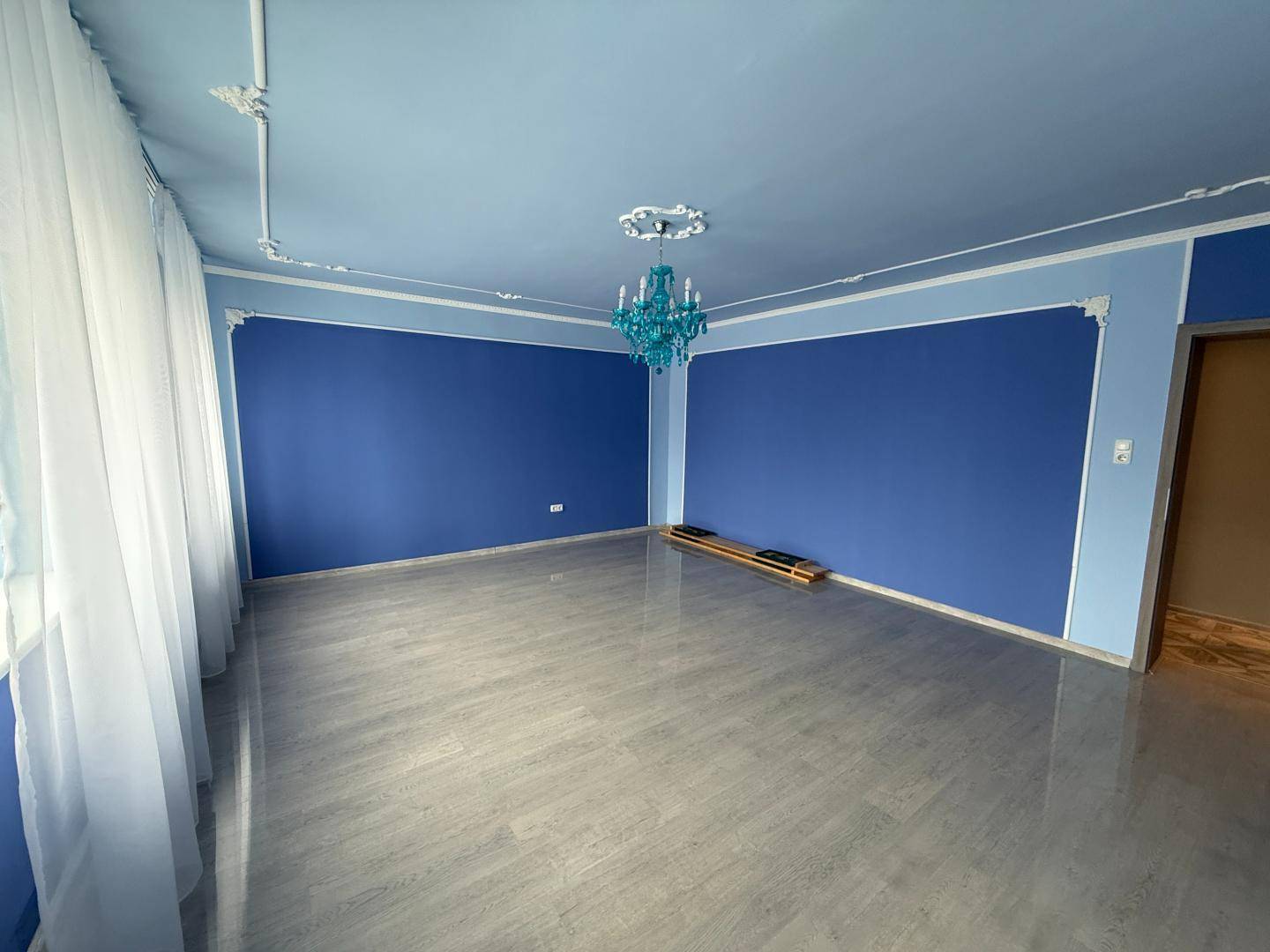 Geräumiges Zimmer mit blauen Wänden, Stuckelementen und modernem Kronleuchter.