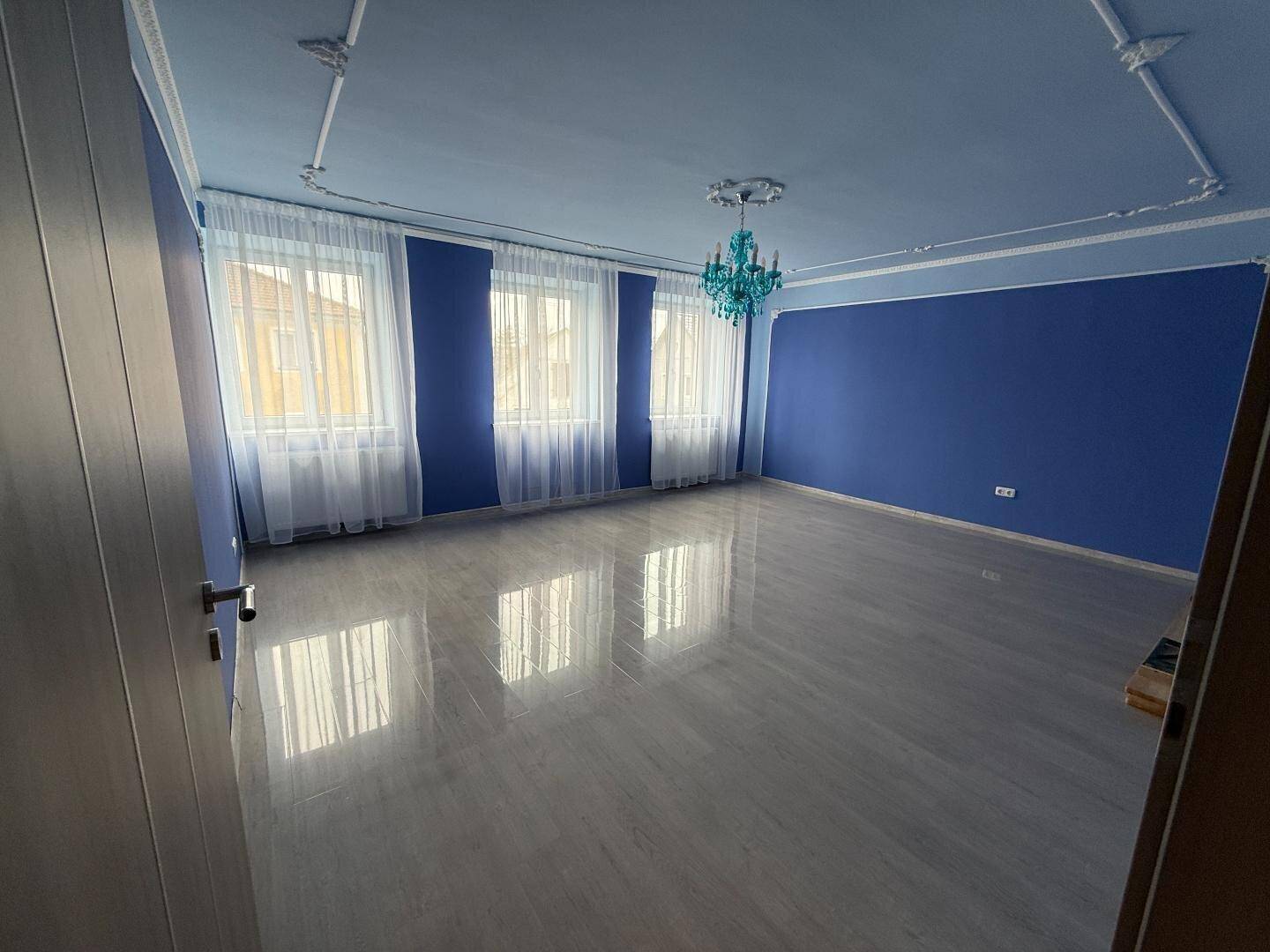 Helles Wohnzimmer mit blauen Wänden, dekorativer Decke und großen Fenstern.