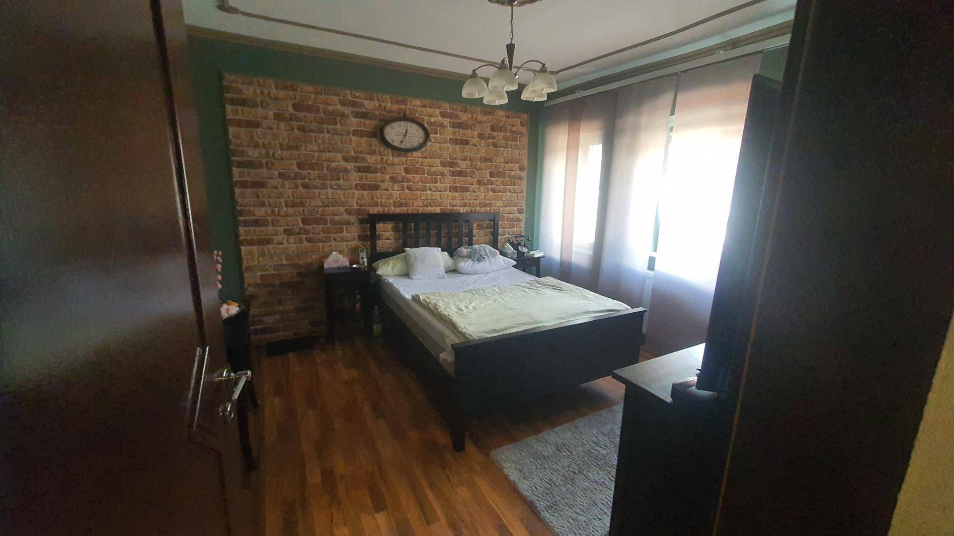 Schlafzimmer mit Holzbett, Ziegelwandakzent und Holzboden.