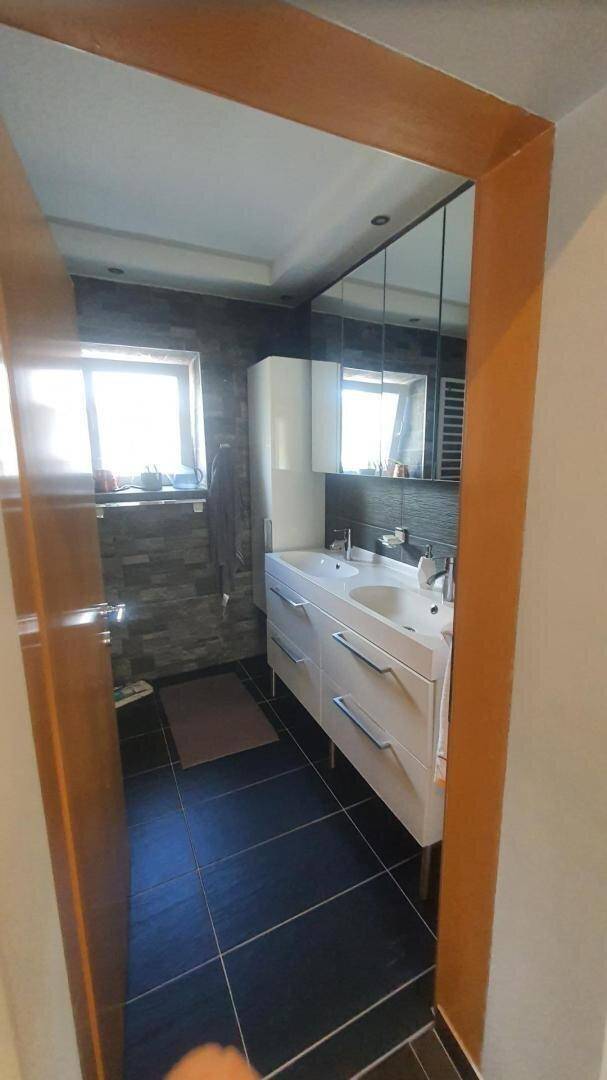 Helles Badezimmer mit Doppelwaschbecken, Spiegelschrank und Fenster.