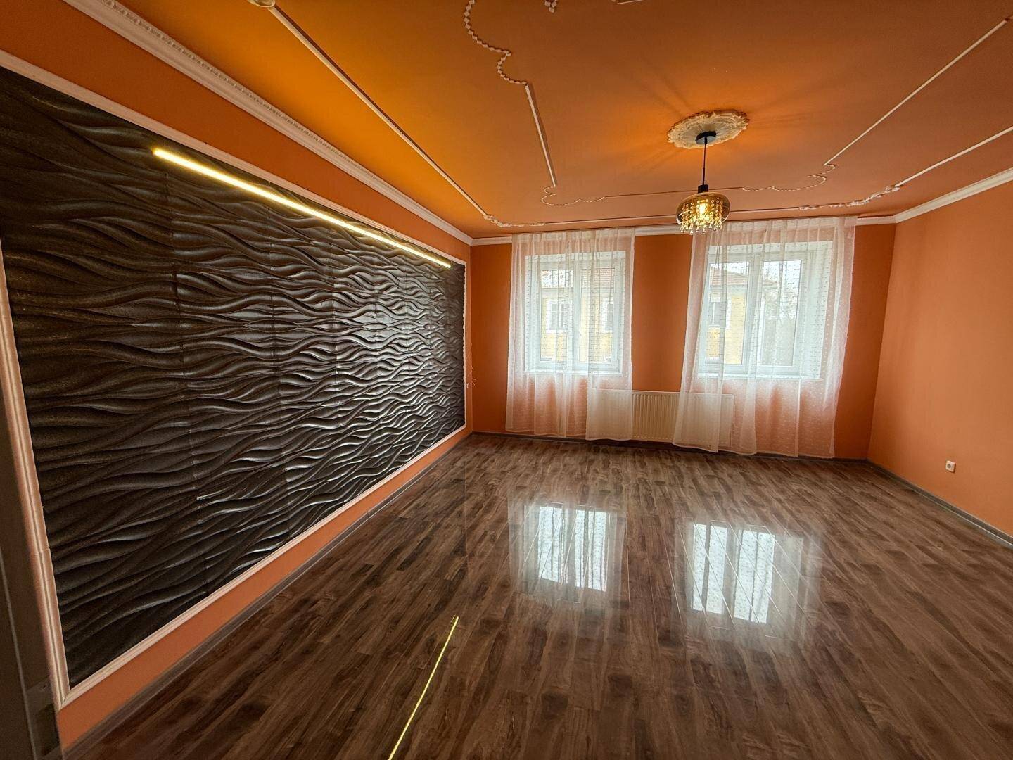 Helles Wohnzimmer mit orangefarbenen Wänden, dekorativer Decke und modernem Wandpaneel.