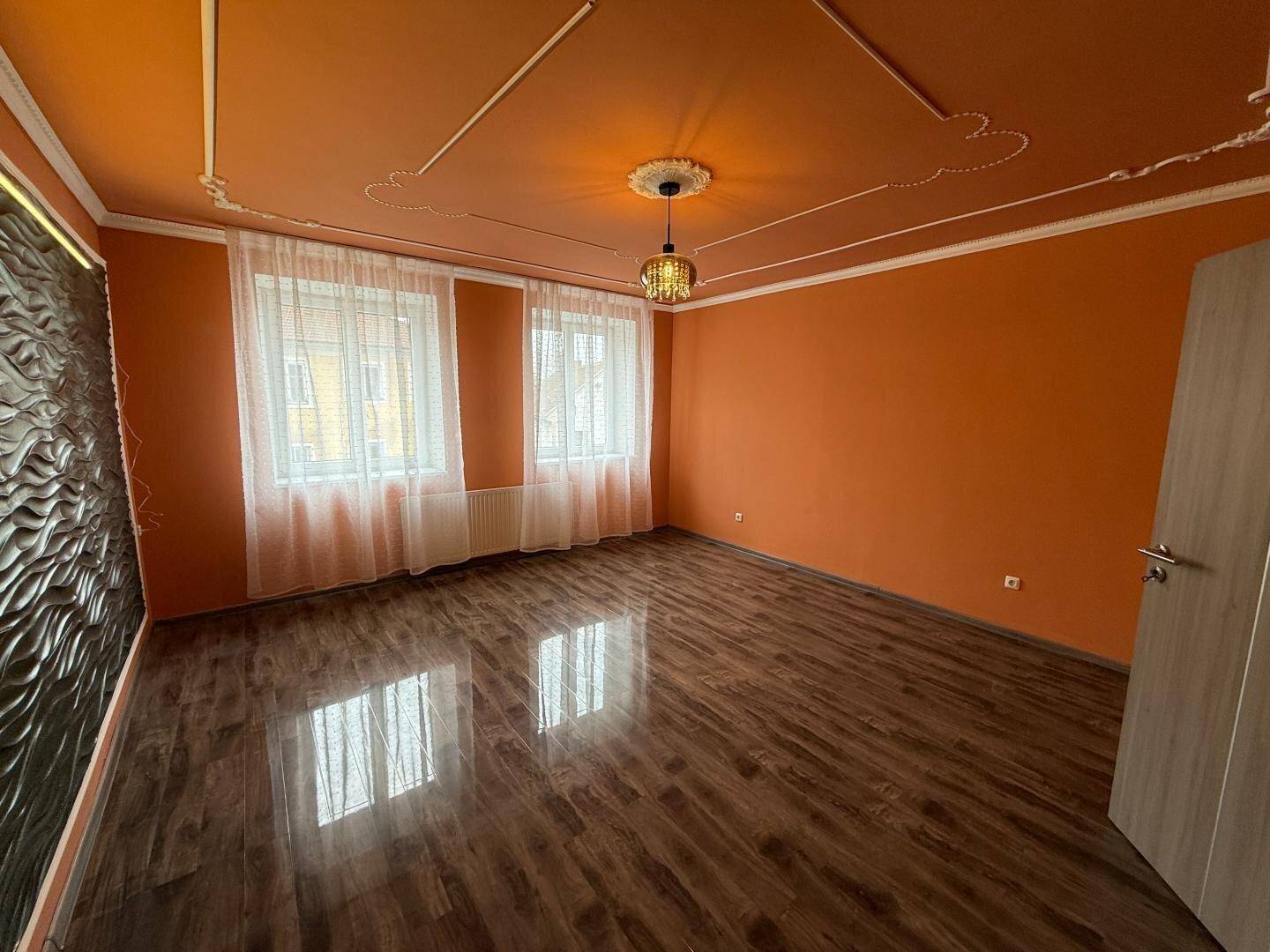 Geräumiges Wohnzimmer mit orangefarbenen Wänden, dekorativer Decke und strukturiertem Wandpaneel.