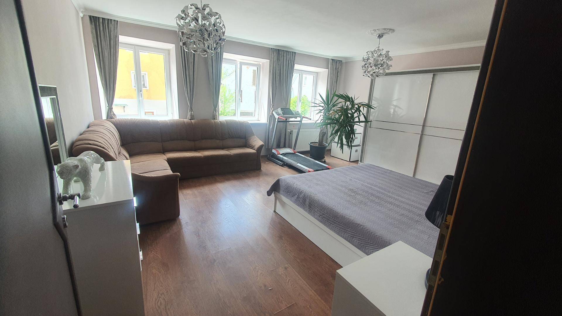 Geräumiges Schlafzimmer mit Bett, Sofa, Laufband und großen Fenstern.