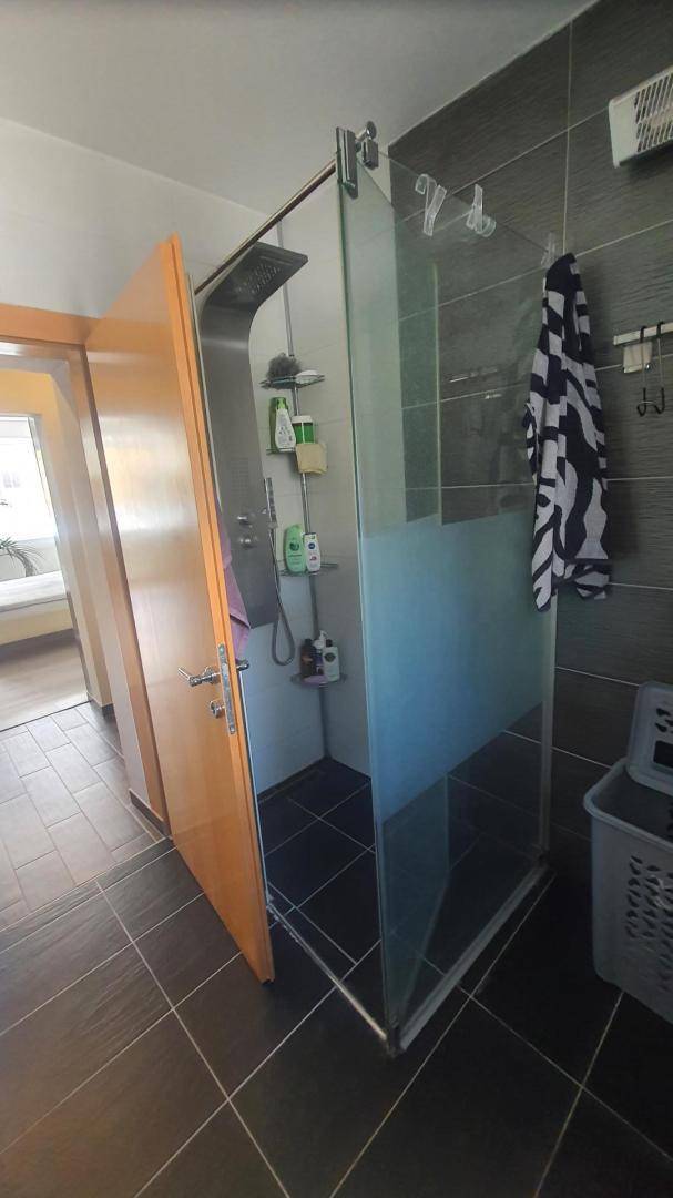 Modernes Badezimmer mit großer begehbarer Dusche und dunklen Fliesen.