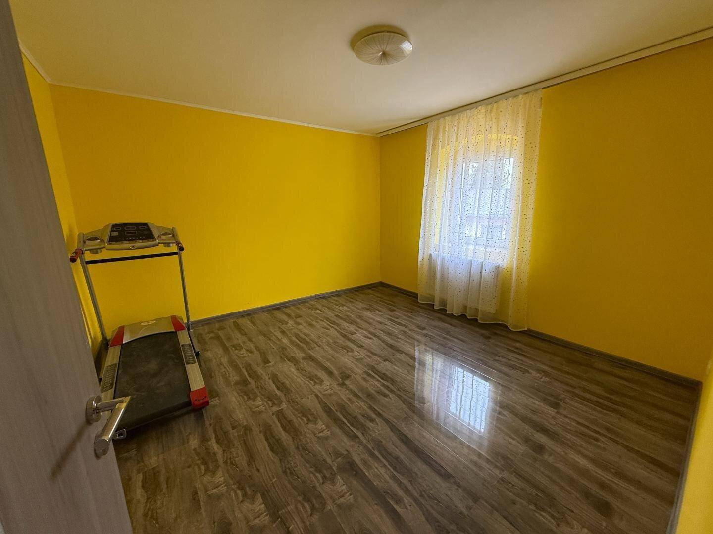 Helles Schlafzimmer mit gelben Wänden, Holzboden und einem Fenster.