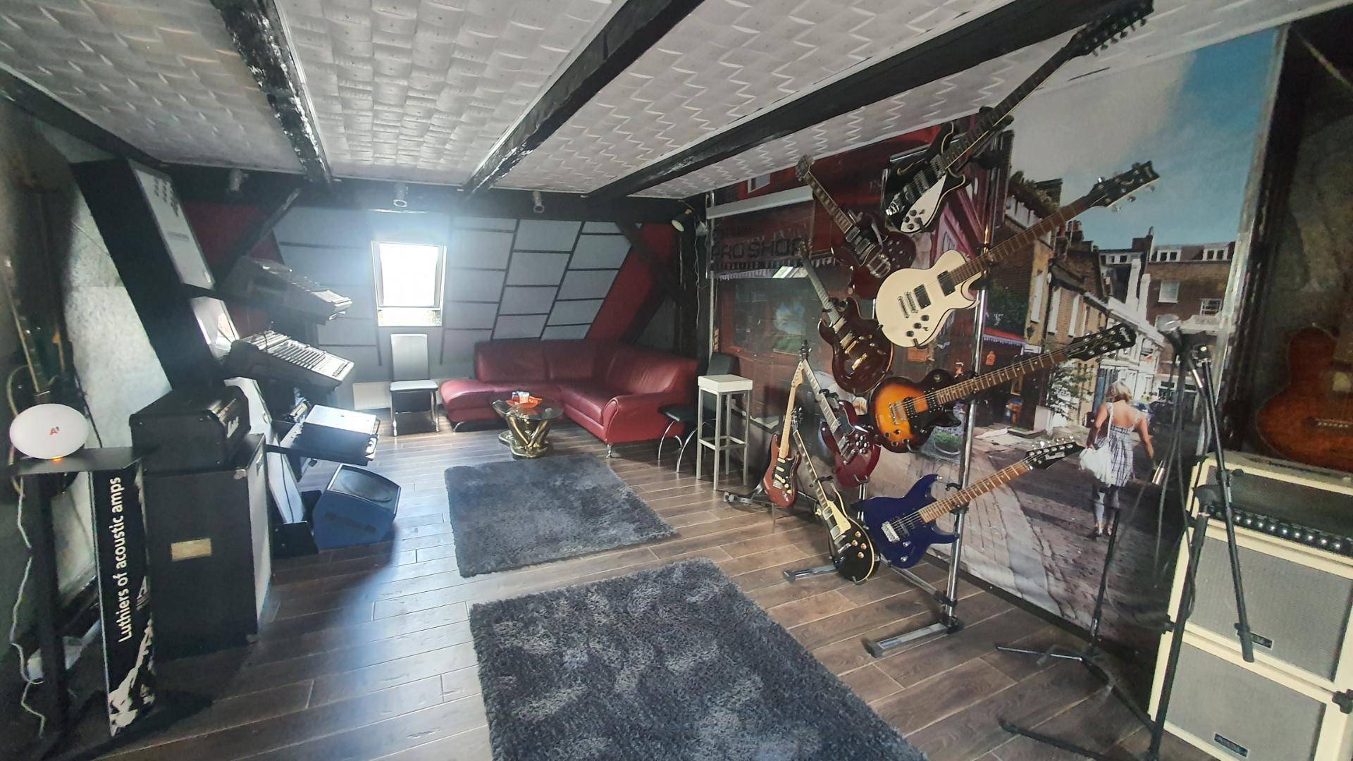Großer Musikraum mit vielen Gitarren, rotem Sofa und Holzbalken.