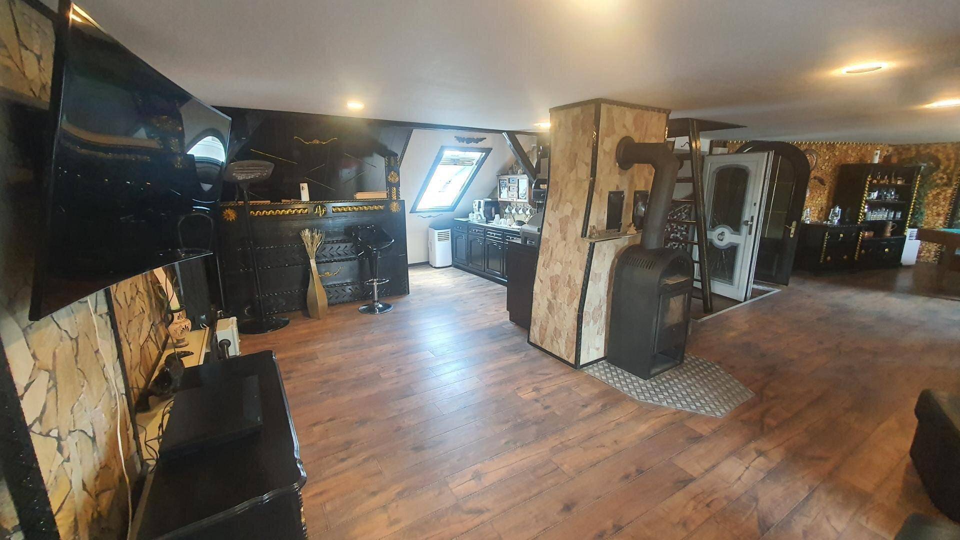 Offener Wohnbereich im Dachgeschoss mit Bar, Kaminofen und Holzboden.
