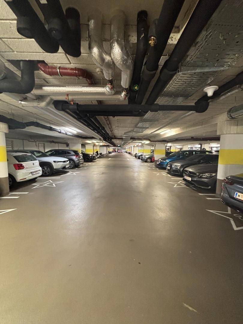 Lange Tiefgarage mit vielen geparkten Autos und sichtbaren Leitungen an der Decke.