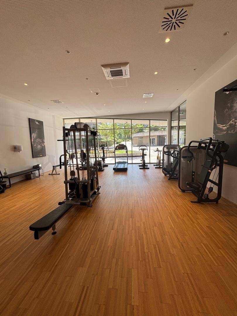Geräumiger Fitnessraum mit verschiedenen Trainingsgeräten und großen Fenstern.
