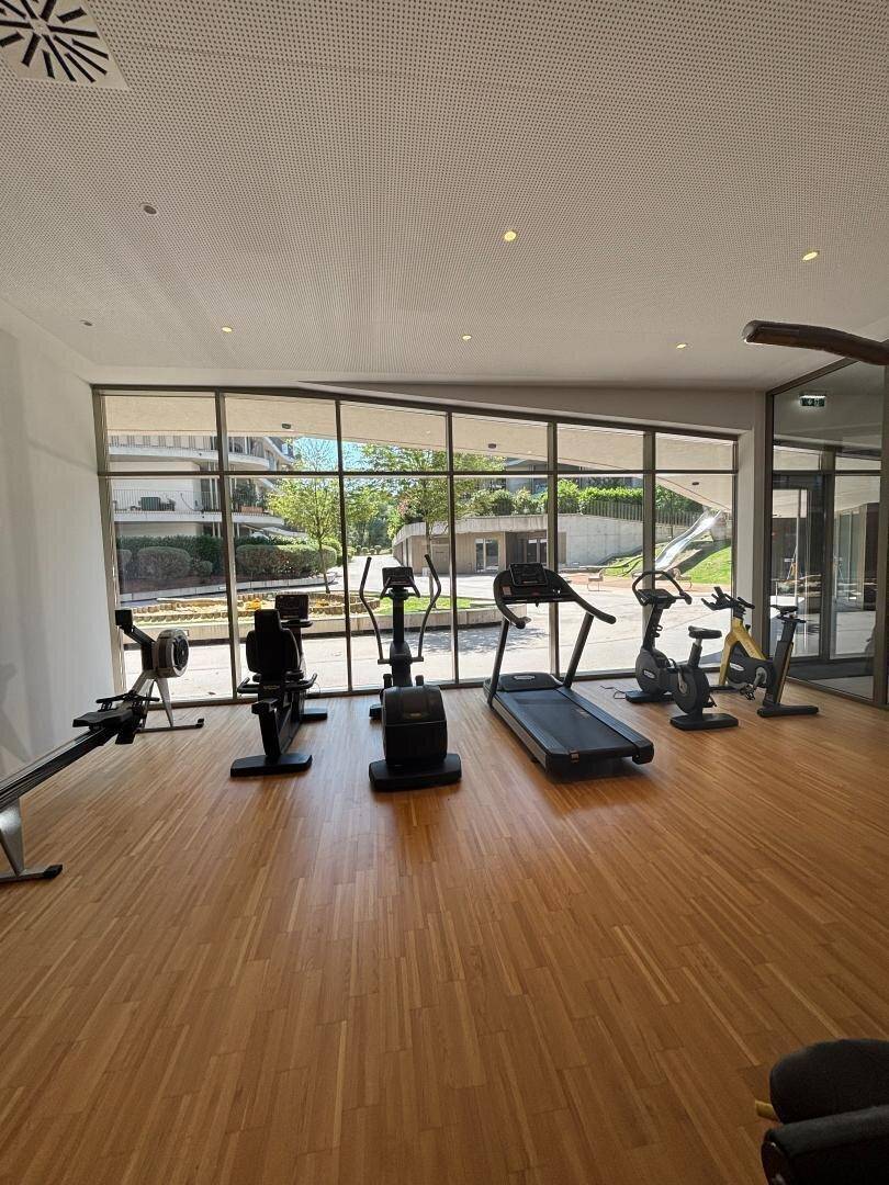 Heller Fitnessraum mit Laufband, Crosstrainer und Blick ins Grüne.